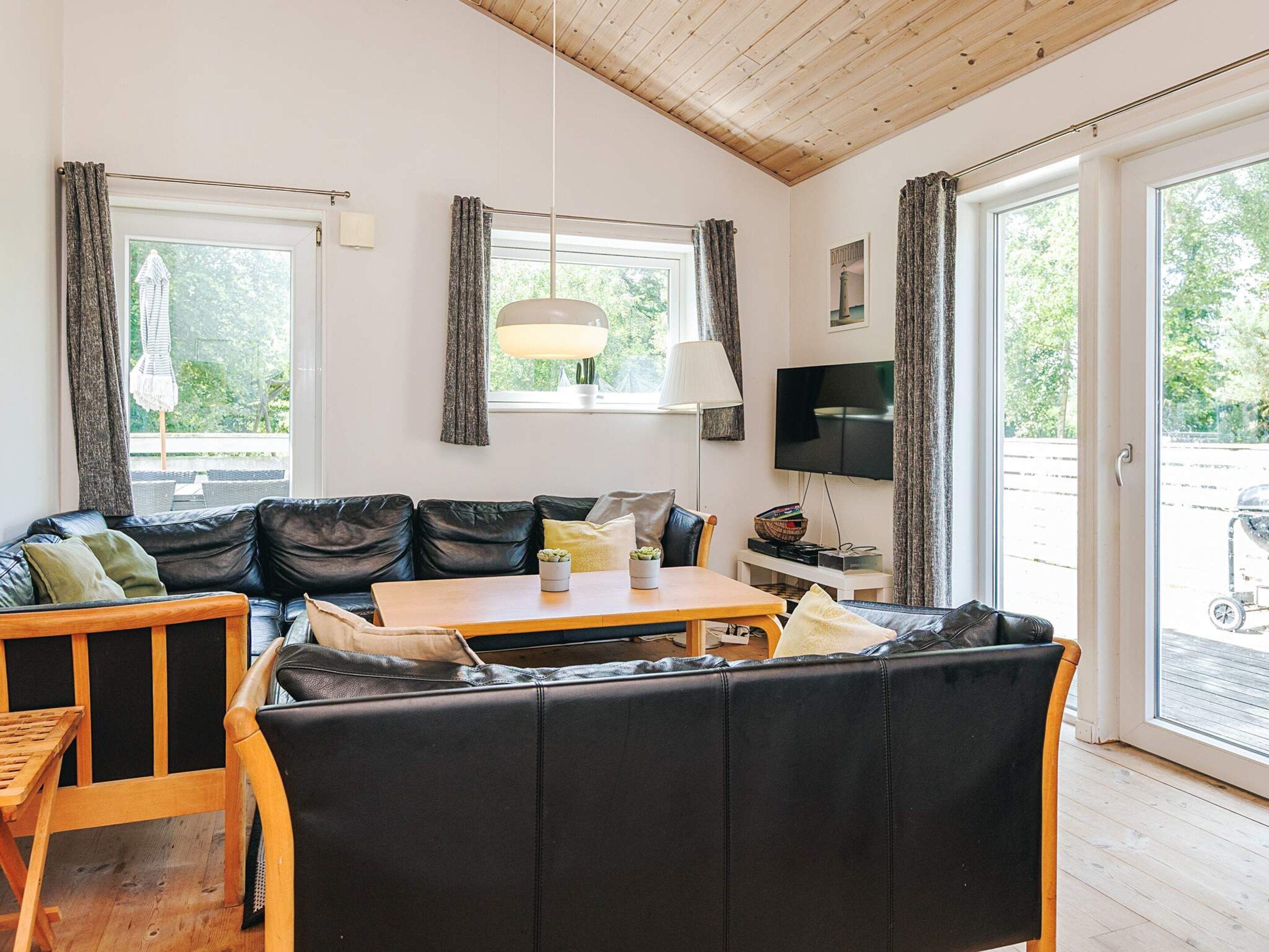 Ein gemütliches Wohnzimmer mit einem schwarzen Ledersofa, einem Holztisch und einem Fernseher an der Wand.