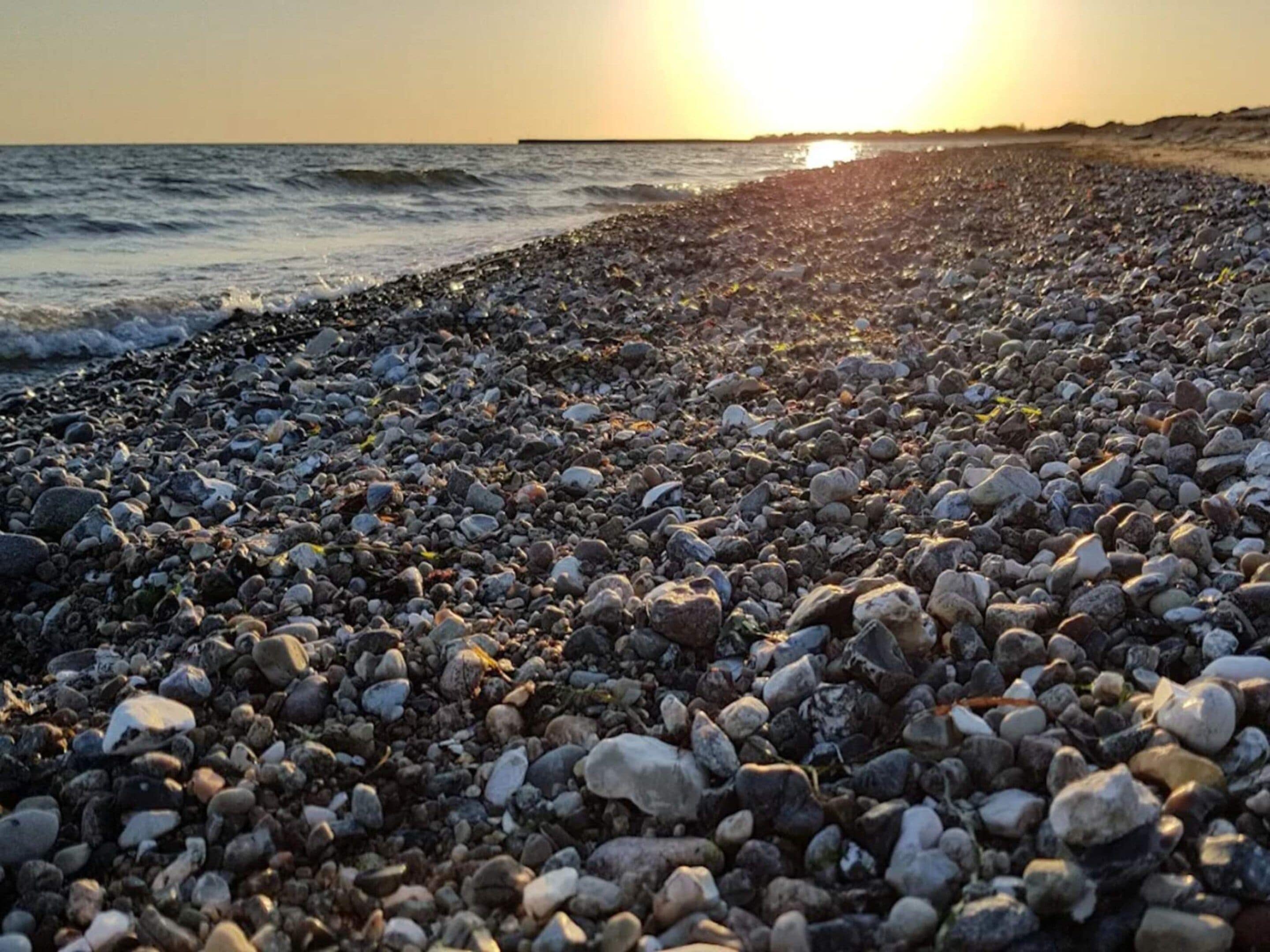 Ein Kiesstrand mit untergehendem Sonnenuntergang im Hintergrund.
