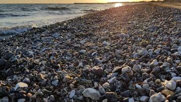Ein Kiesstrand mit untergehendem Sonnenuntergang im Hintergrund.
