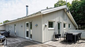Ein modernes Gebäude mit geneigtem Dach, einem Schornstein und einer Terrasse mit Gartenmöbeln.