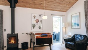 A living room with a wood-burning stove, a sofa, a table with a board game, and a painting on the wall. - 12 Person Holiday Home in Rodby (Rodby)