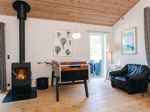 A living room with a wood-burning stove, a sofa, a table with a board game, and a painting on the wall. - 12 Person Holiday Home in Rodby (Rodby)