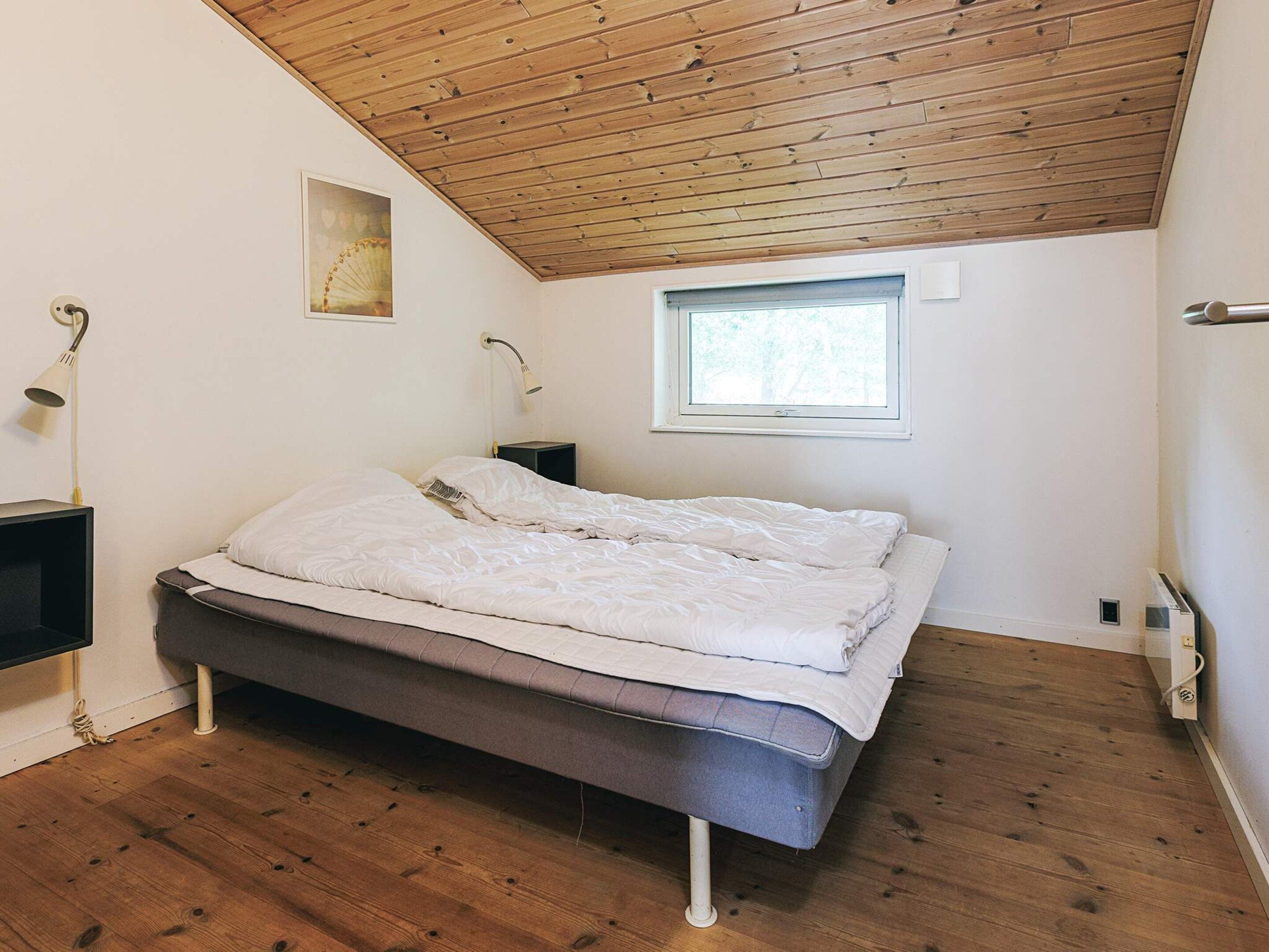 Ein Schlafzimmer mit Holzboden, einem Bett, einem Nachttisch, einer Wandlampe und einem Fenster.