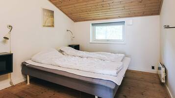 Ein Schlafzimmer mit Holzboden, einem Bett, einem Nachttisch, einer Wandlampe und einem Fenster.
