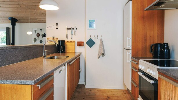 A compact kitchen with wooden cabinets, a built-in oven, a coffee maker, and a hanging towel. - 12 Person Holiday Home in Rodby (Rodby)