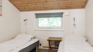 A small, simple room with two single beds, a window with a view of greenery, a wooden ceiling, and a small table with a lamp. - 12 Person Holiday Home in Rodby (Rodby)