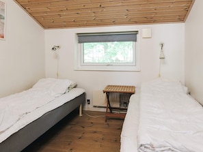 A small, simple room with two single beds, a window with a view of greenery, a wooden ceiling, and a small table with a lamp. - 12 Person Holiday Home in Rodby (Rodby)