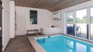 Ein moderner, überdachter Pool mit großen Glaswänden, Holzbalkendecke und Fliesenboden.