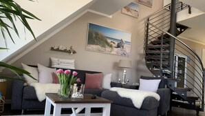 A modern living room with a grey sofa, white coffee table, and a spiral staircase. - Beach Apartment Nordstern (Scharbeutz)