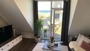 A modern living room with a large sliding glass door leading to a balcony with a view of the beach. - Beach Apartment Nordstern (Scharbeutz)