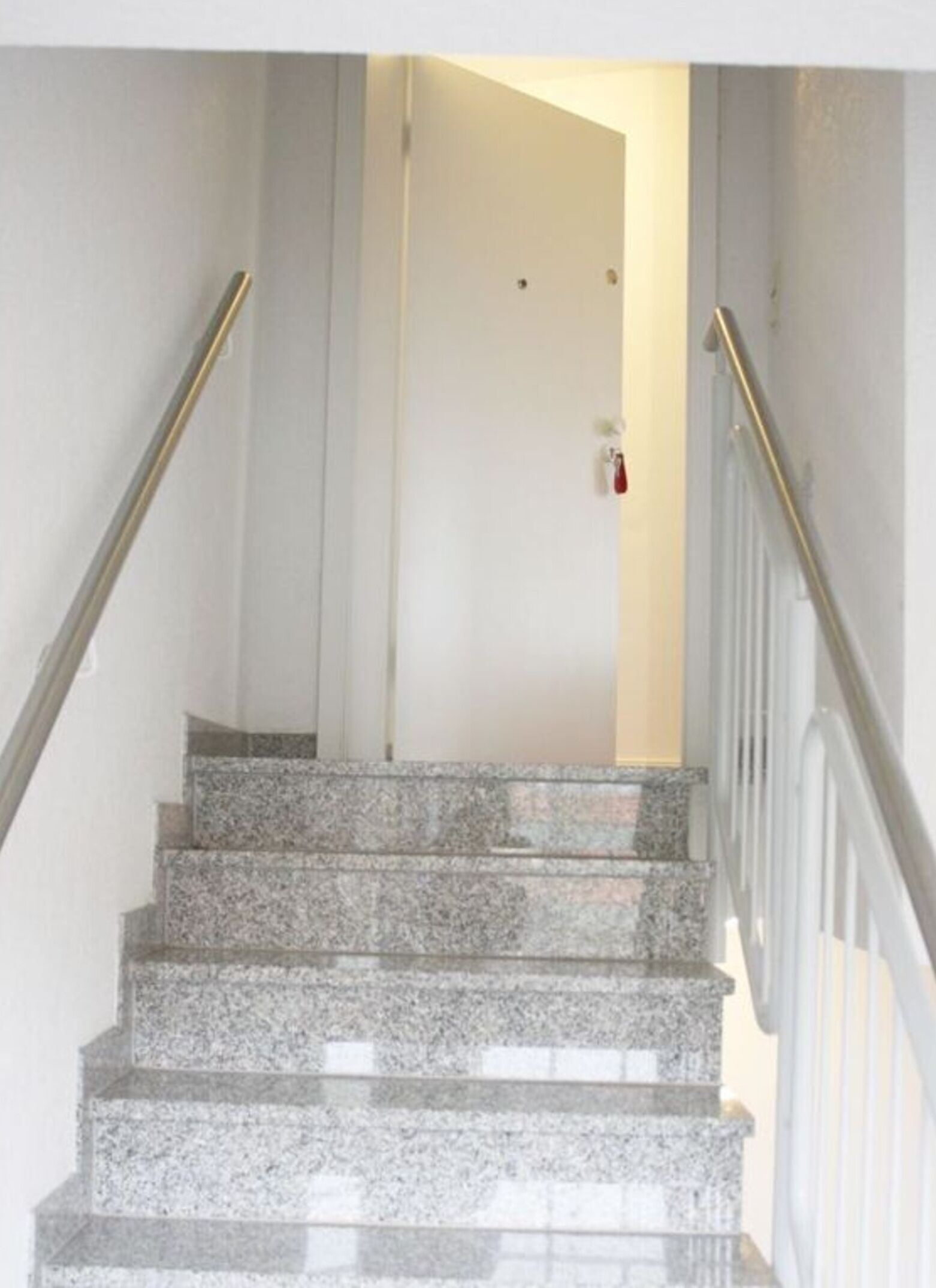 A staircase with granite steps and metal railings, leading to a door with a red handle.