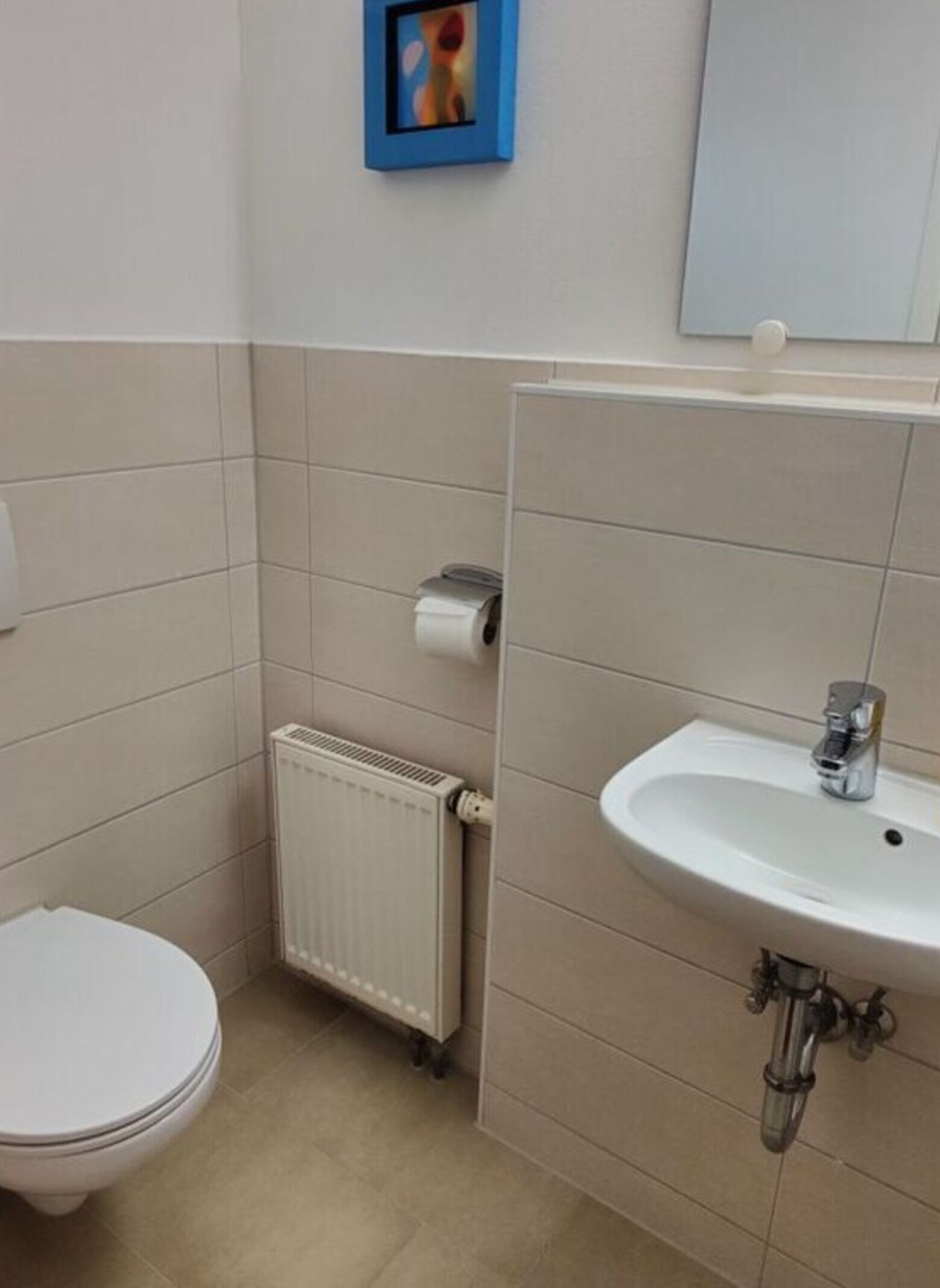 Kylpyhuone, jossa on wc, patteri, pesuallas ja seinällä taulunkehys.