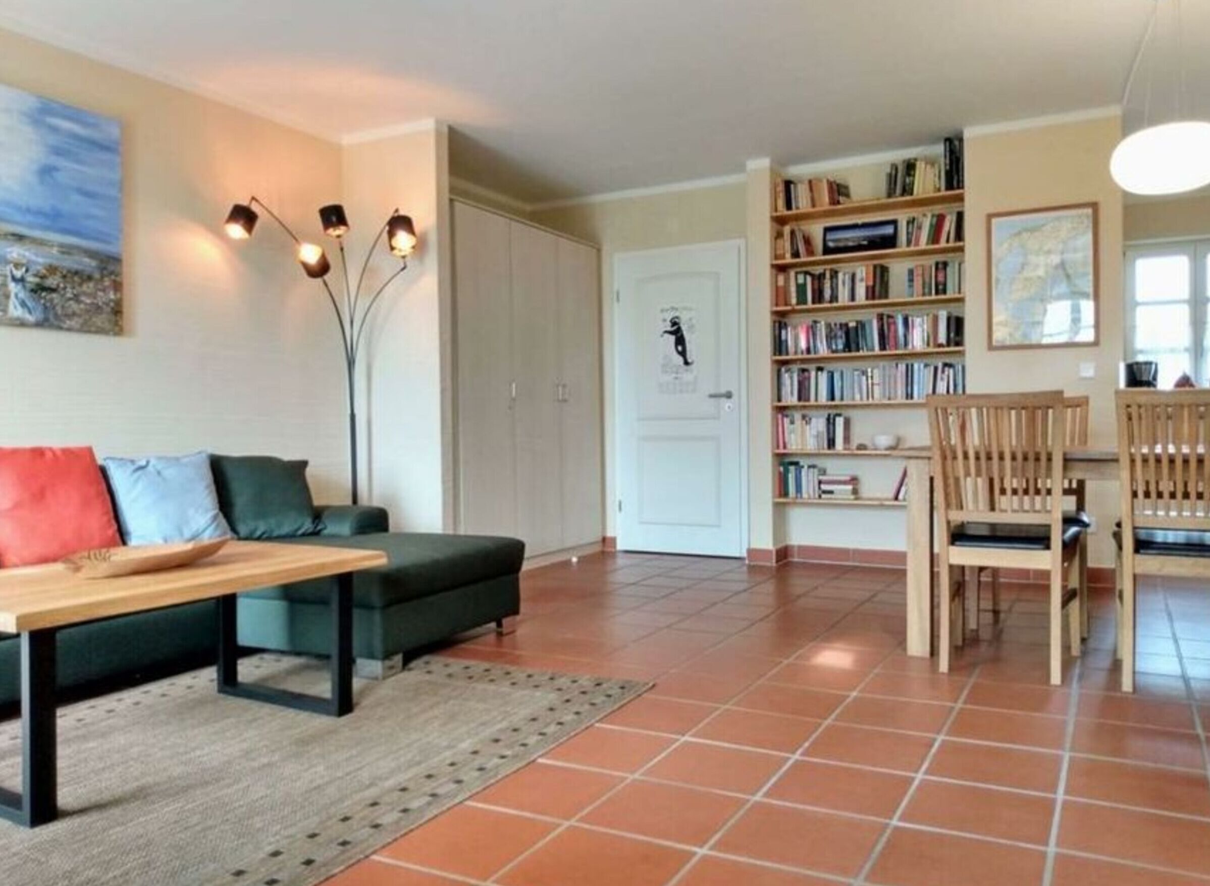 A living room with a sofa, a coffee table, a bookshelf, and a dining area with chairs.