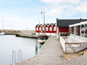 A wooden dock leading to a red building with a flagpole, a boat moored at the dock, and a calm water body. - 3 Person Holiday Home in Traslovslage (Träslövsläge)