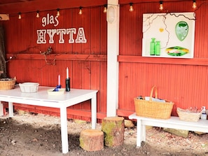 A red wooden structure with a white table and benches, featuring a sign that reads 'glas HYTTA' and a wall with a green bottle and a face illustration. - 3 Person Holiday Home in Traslovslage (Träslövsläge)