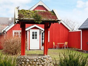 A red barn with a white door, a stone wall, and a small garden area with chairs. - 3 Person Holiday Home in Traslovslage (Träslövsläge)