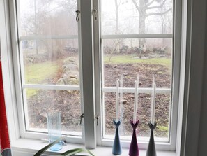 A window with a view of a garden, a glass vase, and three candle holders. - 3 Person Holiday Home in Traslovslage (Träslövsläge)