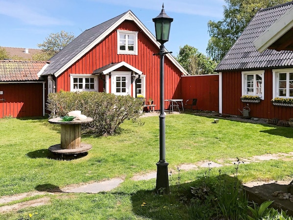 Ett rött hus med ett vitt fönster och en vit d örr, en trädgård med ett bord av sten och en lyktstolpe.