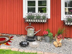 A red building with a window, a metal watering can, a flower pot, and a decorative plate. - 3 Person Holiday Home in Traslovslage (Träslövsläge)
