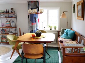 A cozy living room with a wooden dining table, two chairs, a sofa, a bookshelf, and a window with curtains. - 3 Person Holiday Home in Traslovslage (Träslövsläge)