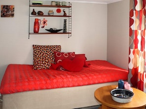 A room with a bed, a round wooden table, and a shelf with decorative items. - 3 Person Holiday Home in Traslovslage (Träslövsläge)