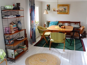 A dining area with a wooden table and chairs, a bookshelf, and a patterned rug. - 3 Person Holiday Home in Traslovslage (Träslövsläge)