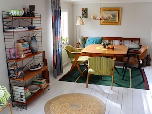 A dining area with a wooden table, chairs, a bookshelf, and a patterned rug. - 3 Person Holiday Home in Traslovslage (Träslövsläge)