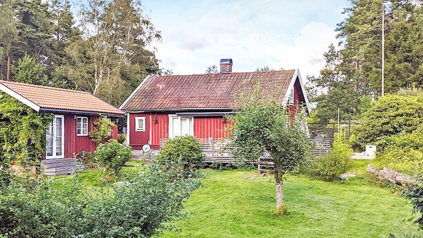 A red barn with a sloped roof, surrounded by a well-maintained lawn and various shrubs. - 4 Star Holiday Home in Jorlanda (Jorlanda)