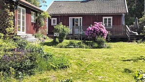 A red wooden house with a tiled roof, a small porch, and a garden with flowers. - 4 Star Holiday Home in Jorlanda (Jorlanda)