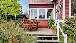 A wooden bench and a small table on a porch with steps leading up to a house with a red exterior and white trim. - 7 Person Holiday Home in Falkenberg-by Traum (Falkenberg)