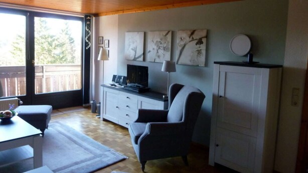 Une pièce avec un plafond en bois, un bureau avec un ordinateur, une chaise, un meuble et une fenêtre donnant sur des arbres.
