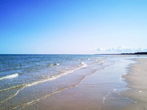 A beach with clear water, a sandy shore, and a distant shoreline with trees. - 4 Star Holiday Home in Hadsund (Hadsund)