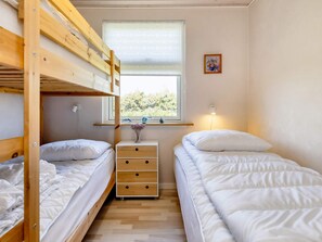 Une chambre avec un lit superposé, une fenêtre, une table de chevet avec une lampe et un petit tableau accroché au mur.
