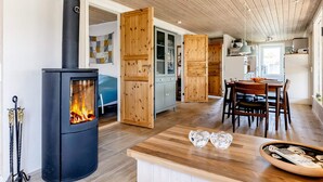 A modern kitchen with a wood-burning stove, a dining area with a wooden table, and a kitchen island. - 4 Star Holiday Home in Hadsund (Hadsund)