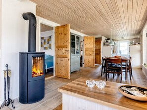 A modern kitchen with a wood-burning stove, a dining area with a wooden table, and a kitchen island. - 4 Star Holiday Home in Hadsund (Hadsund)
