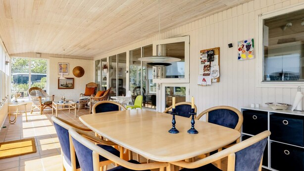 A spacious dining area with a wooden table and chairs, a kitchen area with cabinets, and a view through the glass doors. - 4 Star Holiday Home in Hadsund (Hadsund)