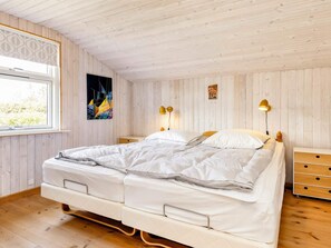 A double bed with a white comforter and pillows, a bedside table with a lamp, and a window with a view of greenery.