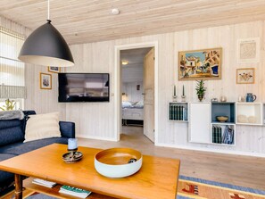 A modern living room with a sofa, coffee table, and a TV. There is a bookshelf with books and decorative items.
