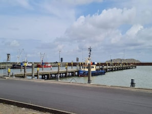 Un muelle costero con varias embarcaciones amarradas, cielo despejado y un promontorio rocoso al fondo.