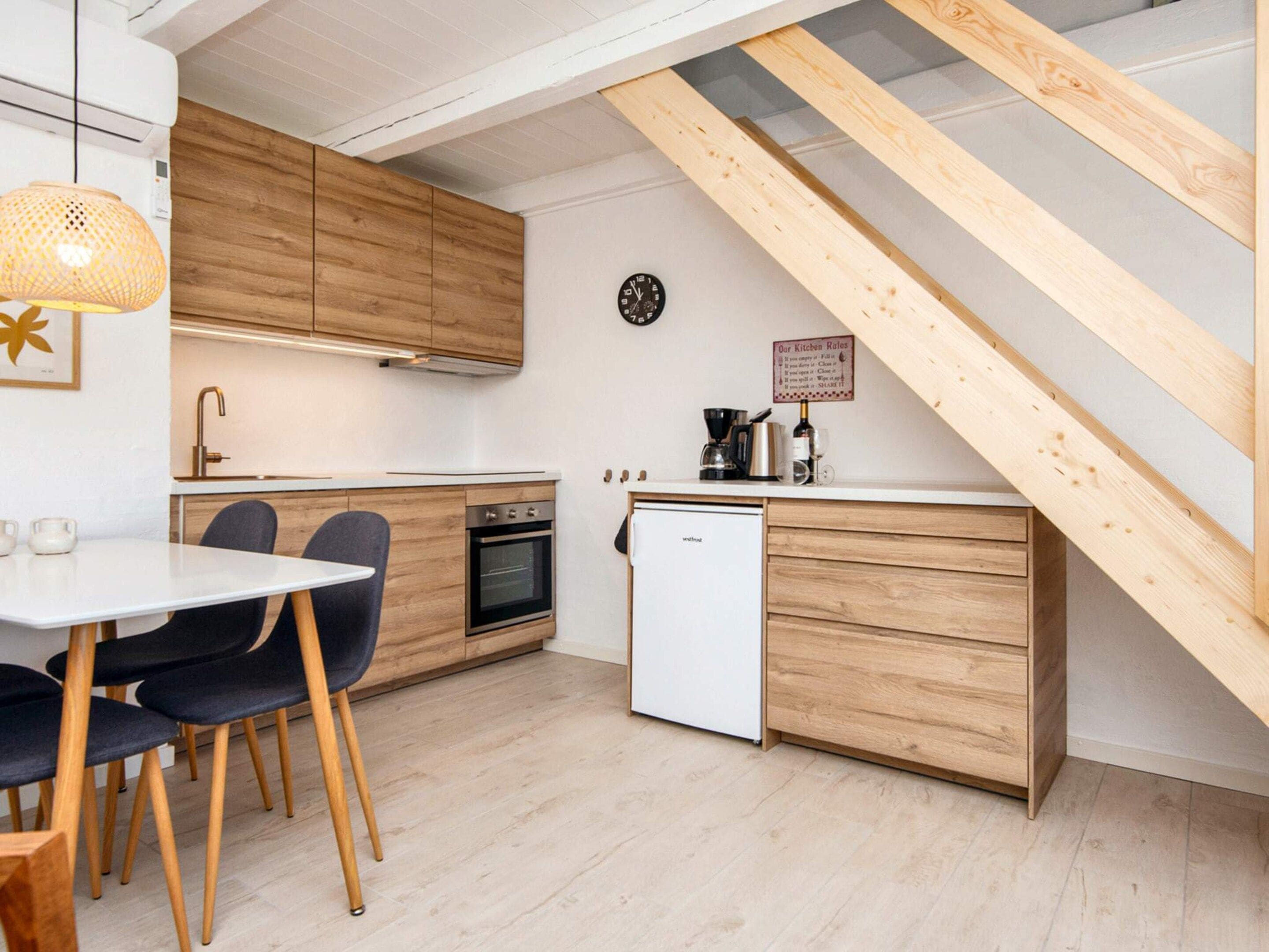Eine kleine Küche mit Holzschränken, einer weißen Arbeitsplatte, einem kleinen Backofen und einem weißen Geschirrspüler.
