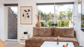 Ein modernes Wohnzimmer mit einem braunen Sofa, einem weißen Beistelltisch, einem gerahmten Kunstwerk und Blick ins Grüne.