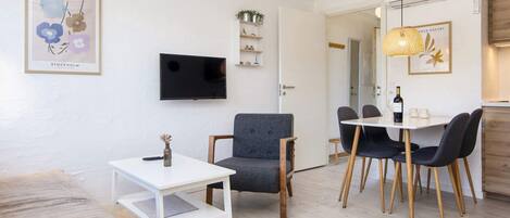 A modern living room with a flat-screen TV, a dining area with a table and chairs, and a sofa.