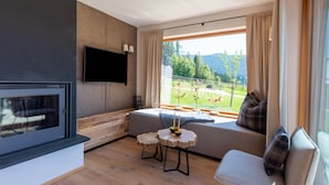 A modern living room with a large TV, a fireplace, a cozy seating area with a view of a green landscape. - Beautiful Chalet With Sauna in Wolting (Tamsweg)