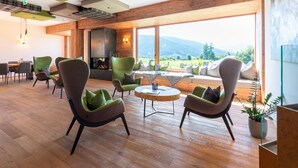 A modern interior with wooden floors, green and grey upholstered chairs, a round wooden table, and a large window offering a mountain view. - Beautiful Chalet With Sauna in Wolting (Tamsweg)