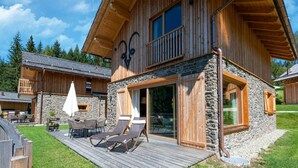 A wooden cabin with a stone foundation, a balcony, and a deck with lounge chairs. - Beautiful Chalet With Sauna in Wolting (Tamsweg)