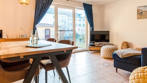A modern living room with a sofa, a TV, and a dining area with a table and chairs. - Holiday Apartment Coastal Love (Ostseebad Wustrow)