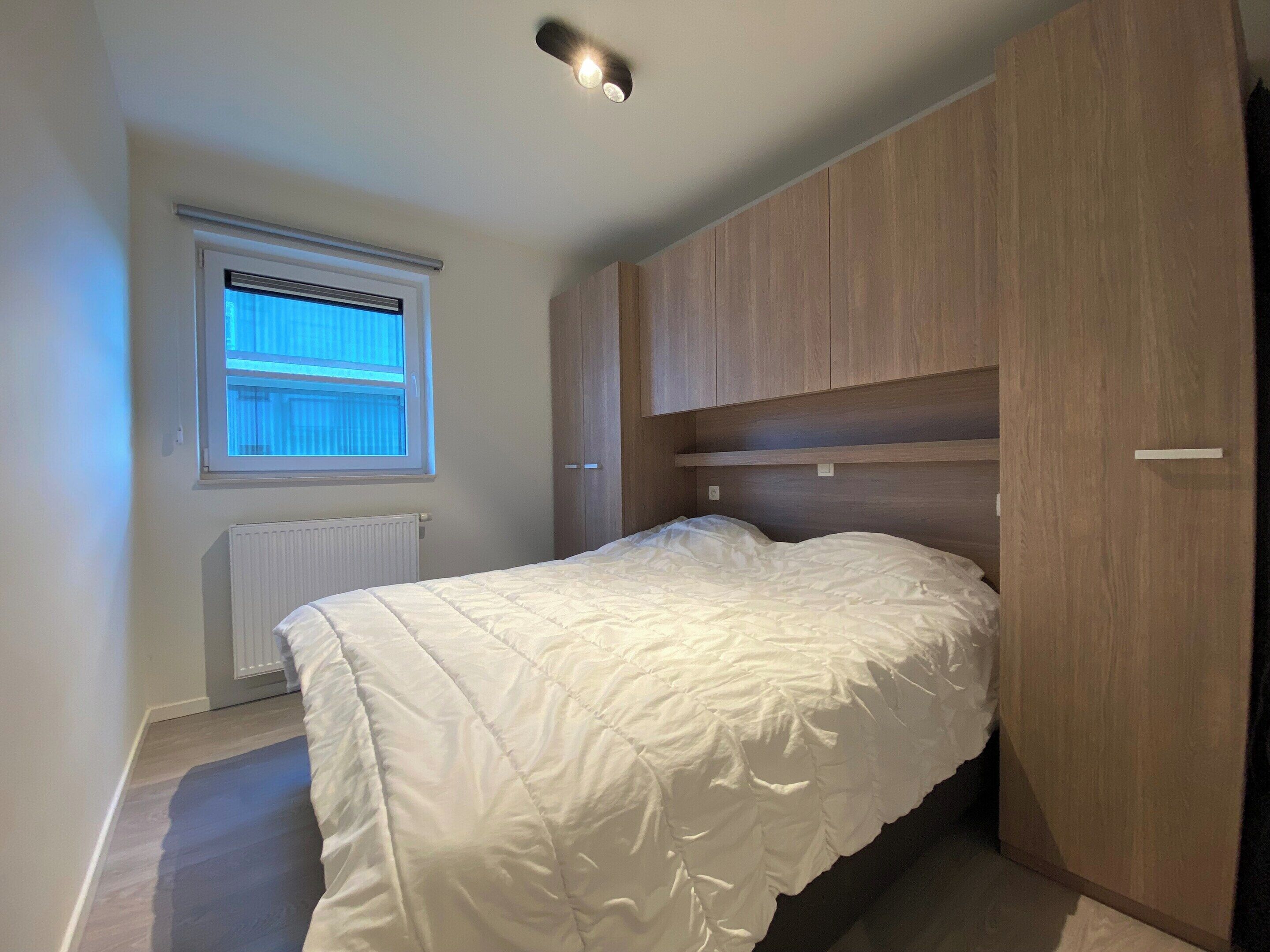 A bedroom with a bed, a window, and built-in wooden storage.