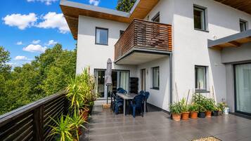 Un bâtiment moderne à deux étages, doté d’un balcon, d’un espace extérieur aménagé pour s’asseoir et de plantes en pot.