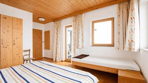 A room with a wooden ceiling, a bed with a striped bedspread, a window with curtains, and a chair. - Apartment in Aschau Near Ski Lift Kaltenbach (Aschau Im Zillertal)