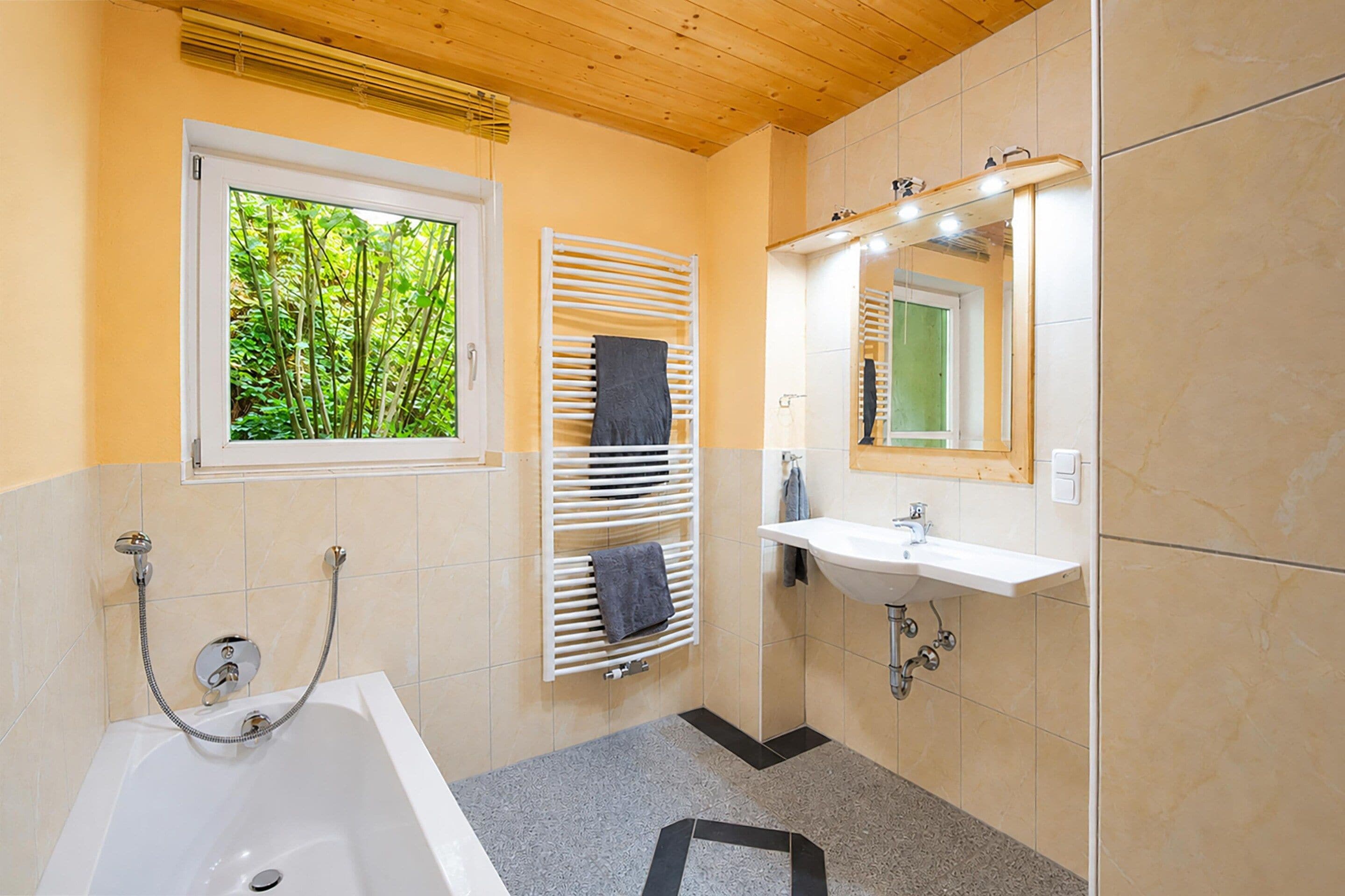 Casa de banho com banheira, janela com vista para vegetação, porta-toalhas e lavatório com espelho.
